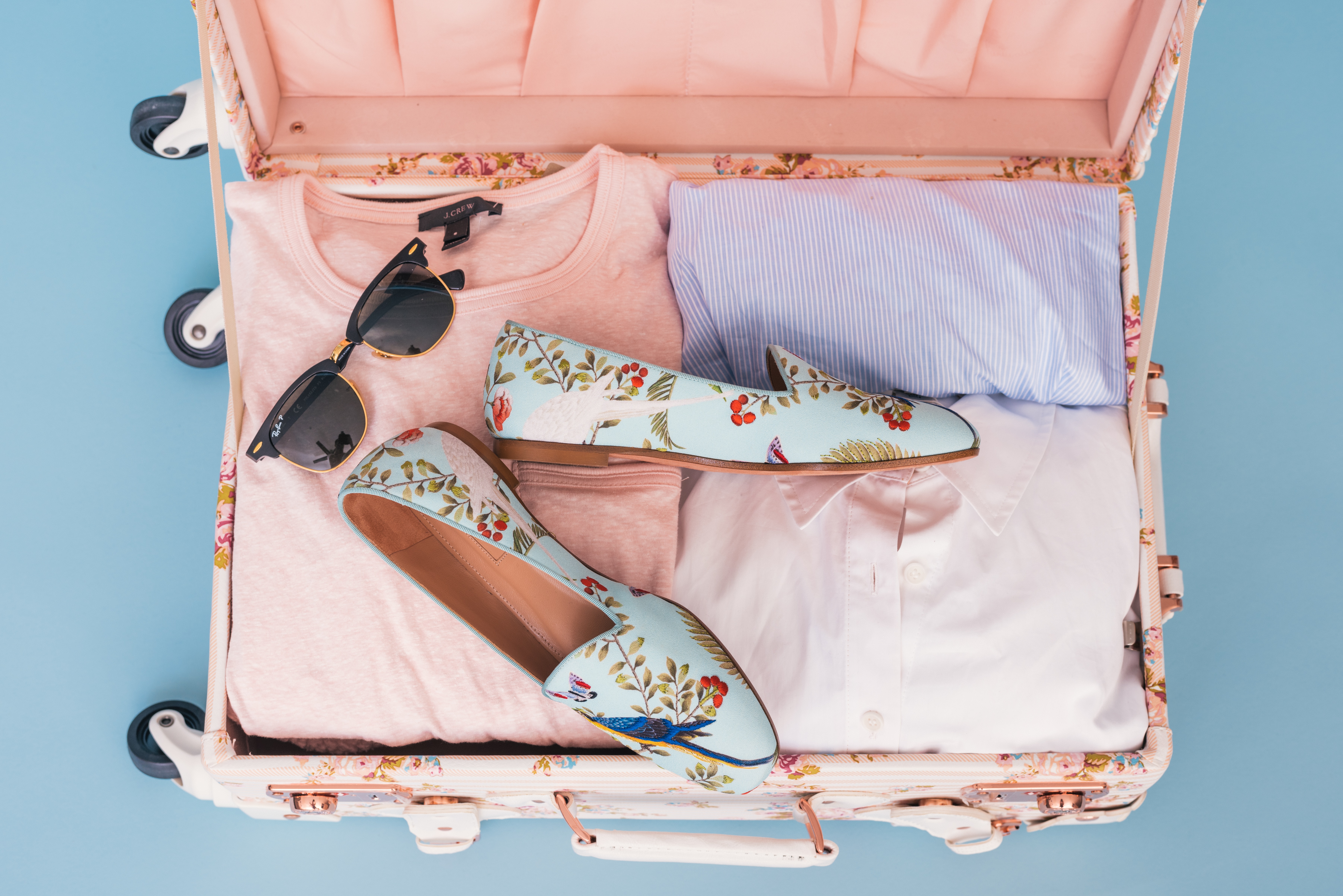 pink suitcase with pink and baby blue clothes shoes and sunglasses